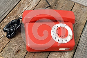 Red vintage landline telephone with dial dial on old wooden dark desk. Classic red telephone.