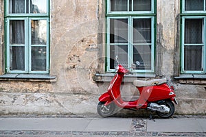 Red vintage scooter on the sidewalk in front of an old brick house