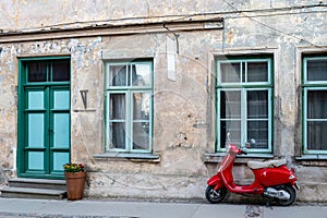 Red vintage scooter on the sidewalk in front of an old brick house