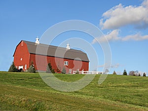 Red vintage wood barn on grassy hilltop under blue sky