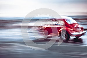 A red volkswagen beetle showing motion blur.