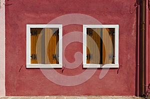 Red wall of Burano Island with two windows, Venice, Italy