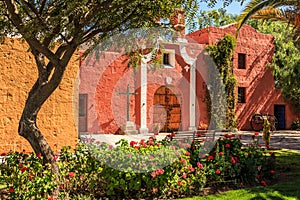 Red walls and gate of Spanish catholic chapel with trees and flo