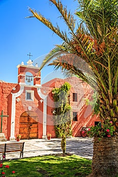 Red walls of Spanish catholic chapel with palms, trees and flowers, Arequipa, Peru