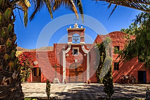 Red walls of Spanish catholic chapel with palms, trees and flowers, Arequipa, Peru