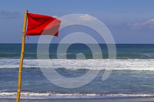 Red warning flag flapping in the wind on beach at stormy weather