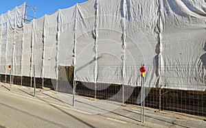 Red warning lights for construction and white scaffold plastic sheeting covering a facade under refurbishment at the roadside.