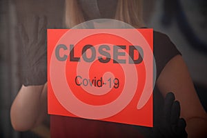 Red warning Sign Closed covid 19 lockdown on front entrance door as new normal shutdown in restaurant. Woman in protective medical