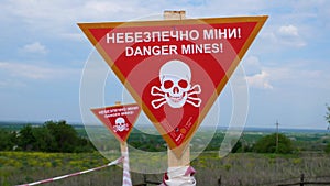 Red warning signs with the inscription Beware of mines near an agricultural field.