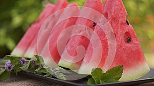 Red watermelon slices on a plate with mint leaves. Camera tilt up.