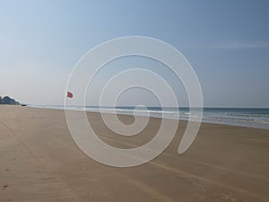 Red waving flag on the sandy beach during morning surf