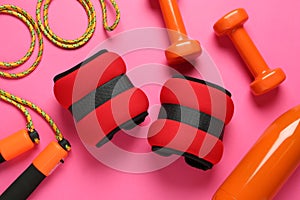 Red weighting agents and sport equipment on pink background, flat lay