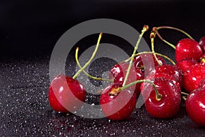 Red wet sweet cherries on black background