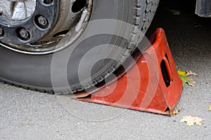 Red wheel chock under the wheel of a car close-up.