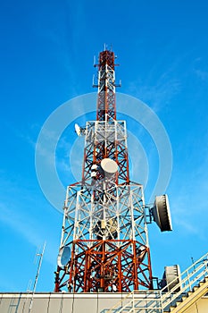 Red and white antenna (cellular tower) under blue sky.