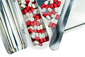 Red, white antibiotic capsules pills with shadow on stainless steel drug tray.