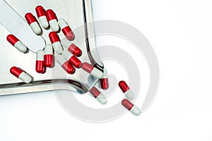 Red, white antibiotic capsules pills with shadow on stainless steel drug tray.