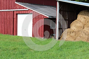 Red and white barn with detached round hay bale storage and green field
