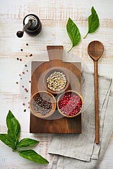 Red, white and black peppers, basil leaves, simple old spoons and linen napkin on old wooden stand. Kitchen accessory concept.