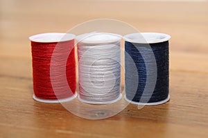 Red white and blue cotton reels or bobbins on a wooden needlework table