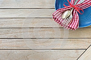 A Red White and Blue Picnic Table Place Setting with napkin, fork and spoon and plate in an upper corner on horizontal wood board photo