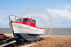 Red, white and blue wooden fishing boat, moored on a pebble beach on a bright summer day