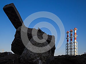 Red-and-white boiler room chimneys against a blue sky. Mountain of stones and debris and pipes boiler station