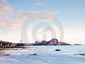 Red white buildings and lighthouse in small port, coastline of cold north sea, Norway.