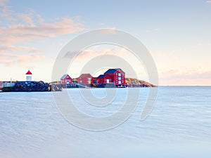 Red white buildings and lighthouse in small port, coastline of cold north sea, Norway.