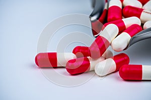 Red-white capsule pills on stainless steel drug tray and some on white table. Pharmacy drugstore background. Pharmaceutics concept