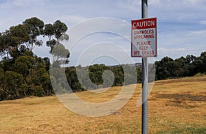 Red and white Caution, Sinkholes Appearing, Please Keep Off The Grass warning sign on a metal pole