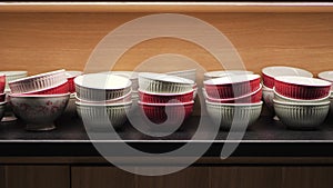 Red and white ceramic bowls in a wooden kitchen cabinet. Tableware lighted from above in a cupboard of modern interior
