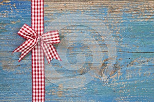 Red/white checkerd bow with a ribbon on wooden blue background f