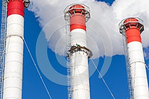 Red-white chimneys of the boiler room, equipped with a traffic light. industrial climbers carry out routine repairs. smoke o