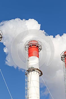 Red-white chimneys of the boiler room, equipped with a traffic light. industrial climbers carry out routine repairs. white smoke