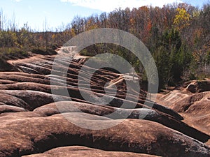 The red and white clay hills of the Cheltenham Badlands formation in Caledon, Ontario, Canada, surrounded by a forest of brightly photo