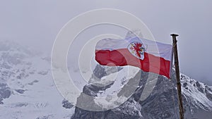 Red and white colored flag of Tyrol with heraldic animal flying in wind near mountain refuge SchaubachhÃ¼tte.
