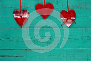 Red and white country hearts hanging by ribbon on antique teal blue sign