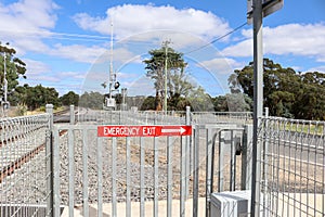 Red and white Emergency Exit sign with arrow on a gate at a pedestrian crossing