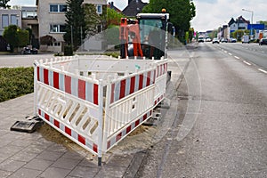 Red-white fence during repair work on a city road. Small excavator in the background