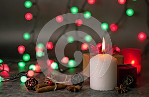 Red and white festive candles burn with a yellow flame on a table among gifts in craft paper, rattan balls, cinnamon sticks and