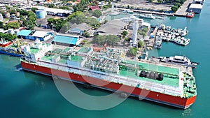 Red and white Floating Storage and Regasification Unit, FSRU, LNG-vessel in Benoa Harbour under light blue sky.