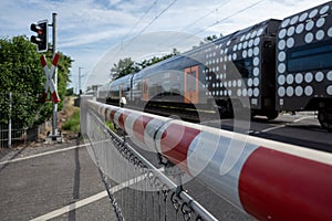 Red and white level crossing railway barrier which block the road and regional train move on the railway.