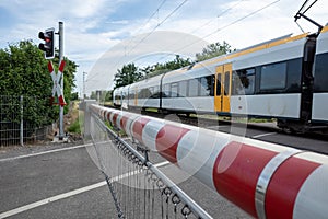 Red and white level crossing railway barrier which block the road and regional train move on the railway.