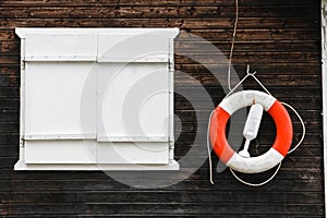 Red and white lifebuoy lifebelt with ropes hanging from a dark brown painted wooden wall