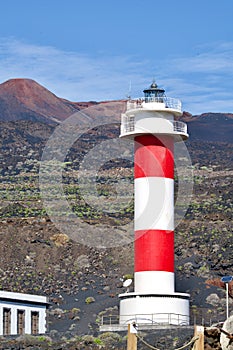 Red-white light house in font of a volcano