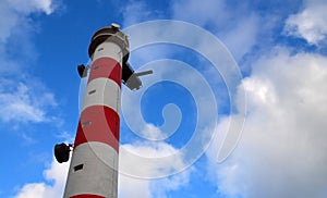 Red and white lighthouse against blue sky with clouds.