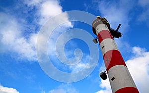 Red and white lighthouse against blue sky with clouds.