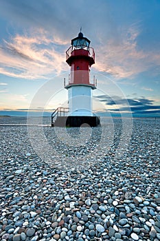 Red and white lighthouse on a beach with pebbles