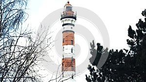 Red and white lighthouse, in winter the trees in the foreground